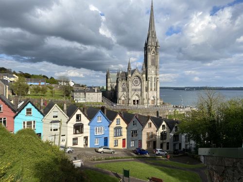 Free Gothic architecture of St. Colman's Cathedral against a vibrant row of houses in Cobh, Ireland by the sea. Stock Photo
