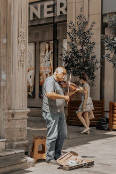 Elderly street musician plays violin on bustling city sidewalk.