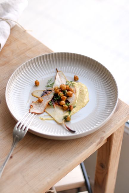 A stylish gourmet dish with roasted chickpeas and garnish on a wooden tabletop, captured in natural light.