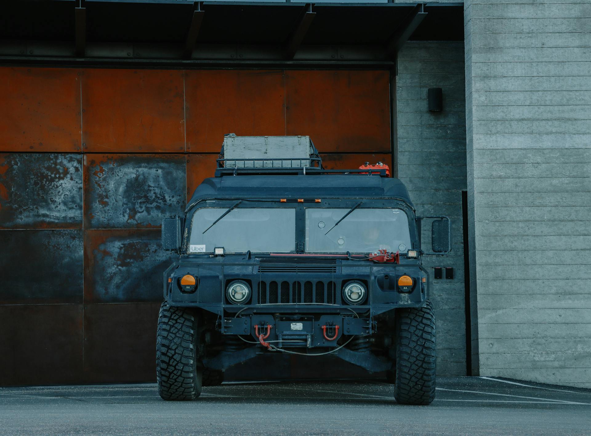 A rugged military vehicle is parked outside a rustic metal garage, showcasing its robust design.