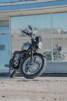 A sleek, vintage motorcycle parked outdoors with reflection in urban glass building.