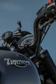 Detailed view of Triumph motorcycle handlebars with speedometer against clear sky.