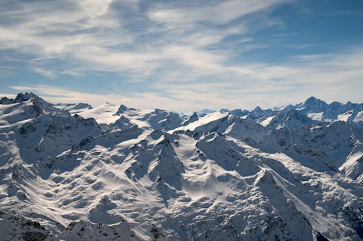Majestic aerial view of snow-capped mountain peaks under a bright sky.