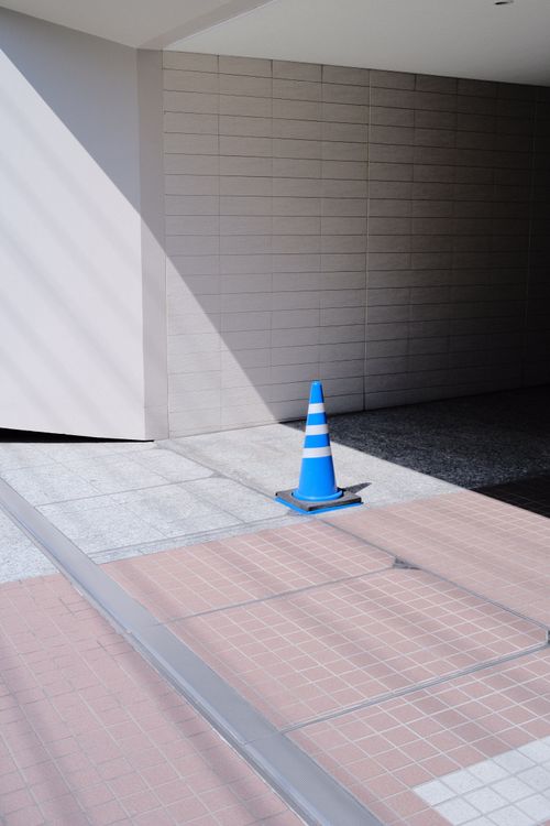 Free A blue traffic cone casts a shadow on a sunlit urban sidewalk, conveying a minimalist urban scene. Stock Photo