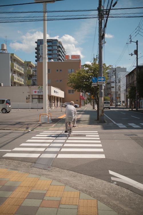 Free A man rides a bicycle across a zebra crossing in a modern urban townscape under clear skies. Stock Photo
