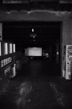 Black and white image of a warehouse interior with a truck, creating a moody urban atmosphere.