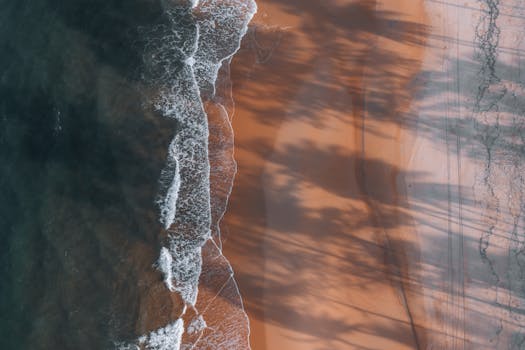 Stunning aerial shot of Kijal Beach with waves meeting the sandy shoreline and tree shadows casting beautiful patterns.