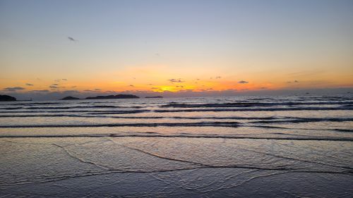 Free A peaceful beach scene with the sun setting over gentle ocean waves. Stock Photo