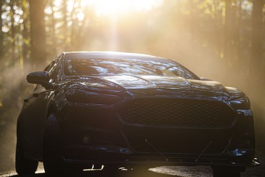 A black car captured with sunlight streaming through a forest, enhancing its grille and hood.
