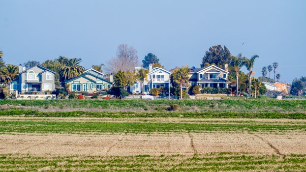 A picturesque view of suburban homes lined up beyond an expansive grass field on a clear day.