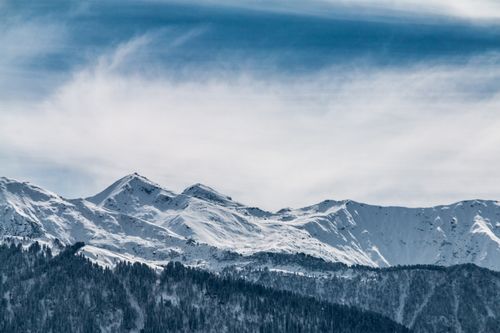 Free A scenic view of snow-capped mountains beneath a cloudy winter sky, offering a serene and cold environment. Stock Photo