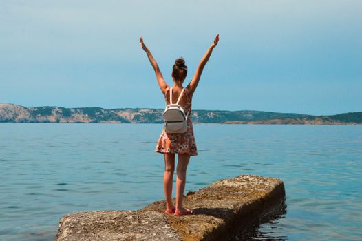 Woman in floral dress with arms raised, enjoying the view by the sea in Croatia.