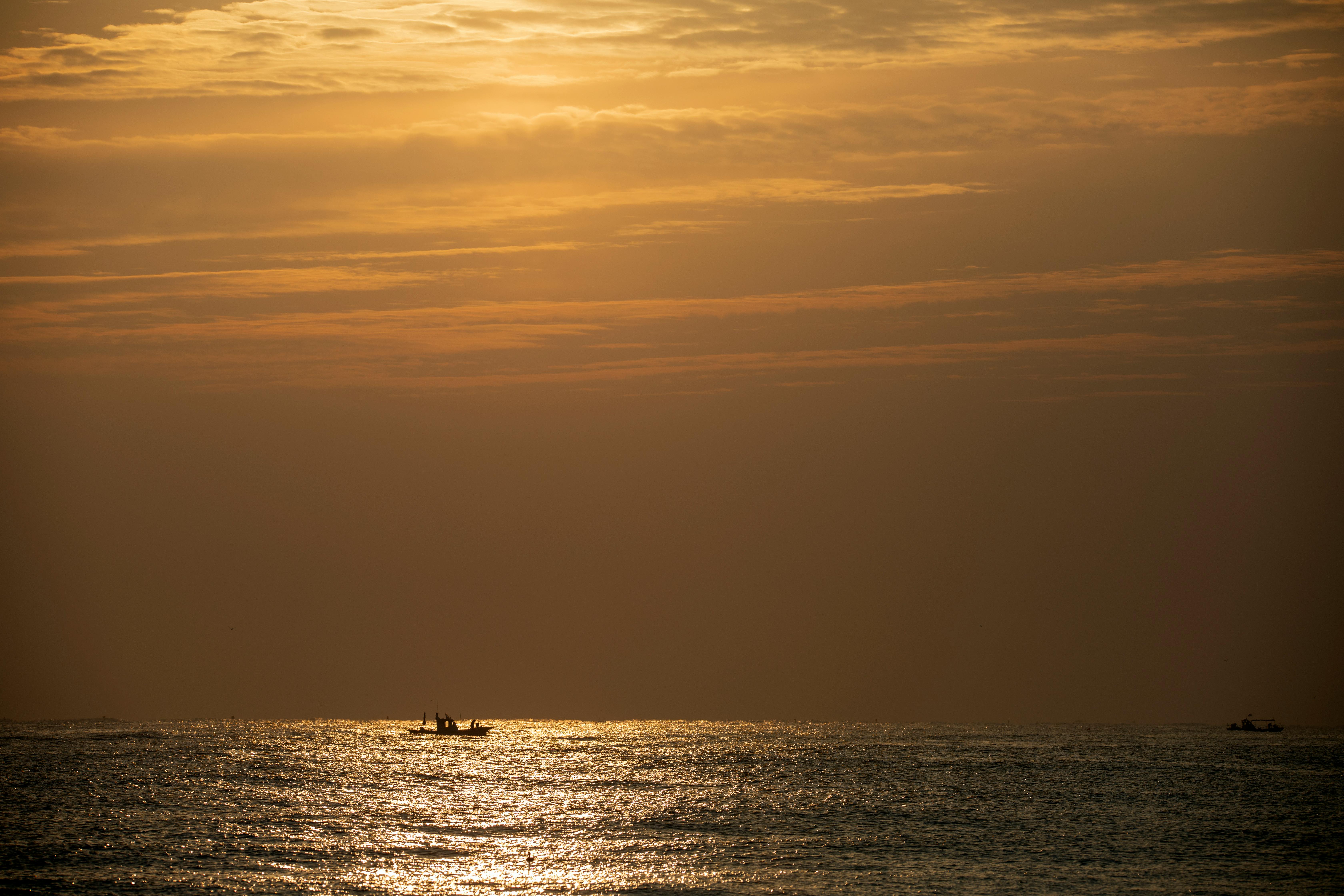 A tranquil scene of a silhouette boat sailing at sunset on the South Korean sea, creating a peaceful ambiance.
