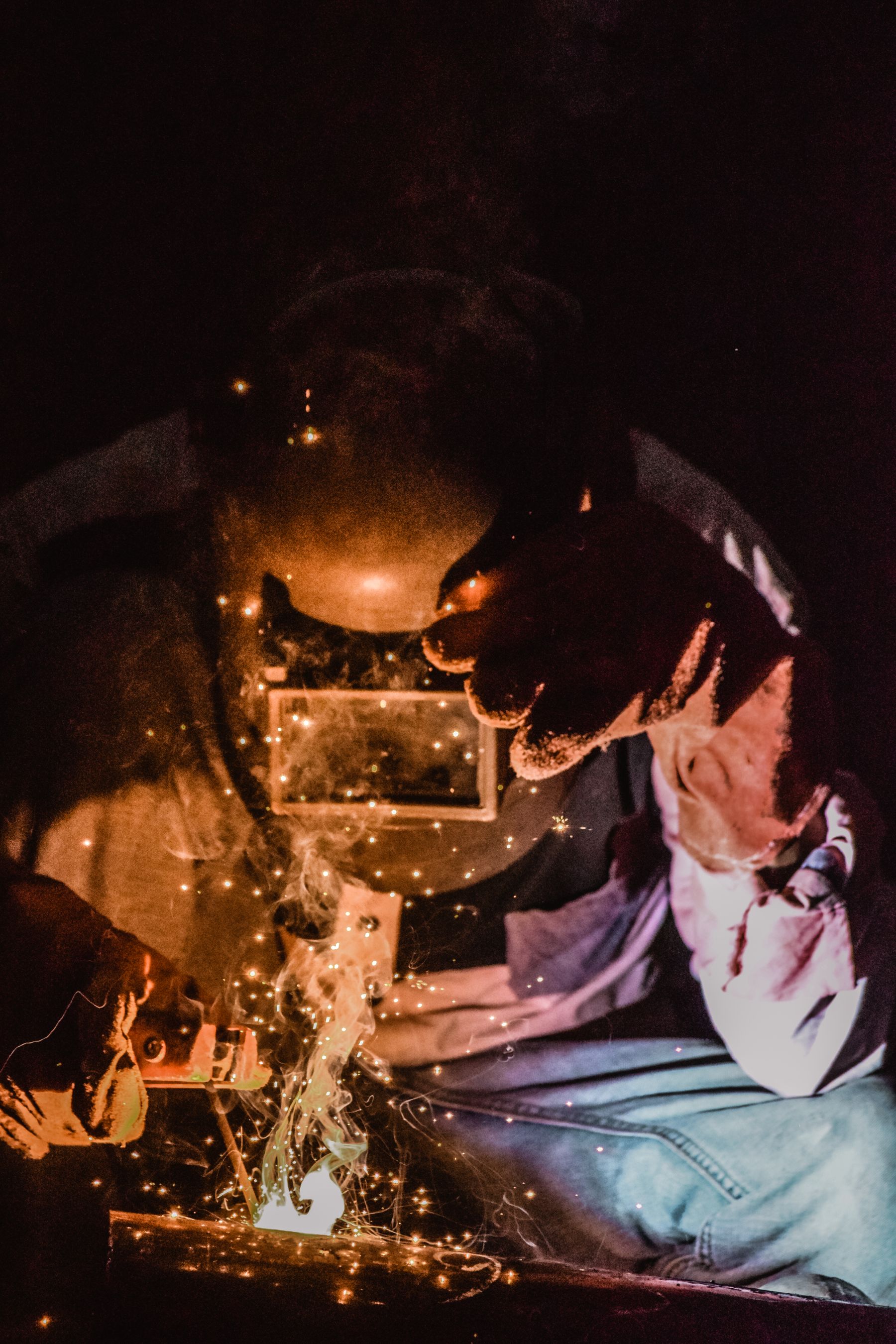 Close view of a welder at work, arc light and sparks off the joint.