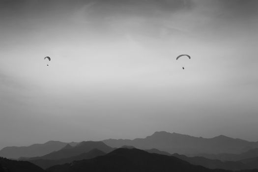 Dramatic paragliding scene over misty mountains captured in black and white.