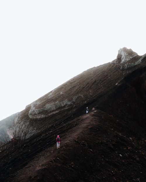 Free Two hikers ascend a rugged mountain trail in Indonesia, capturing the essence of adventure in a dramatic landscape. Stock Photo