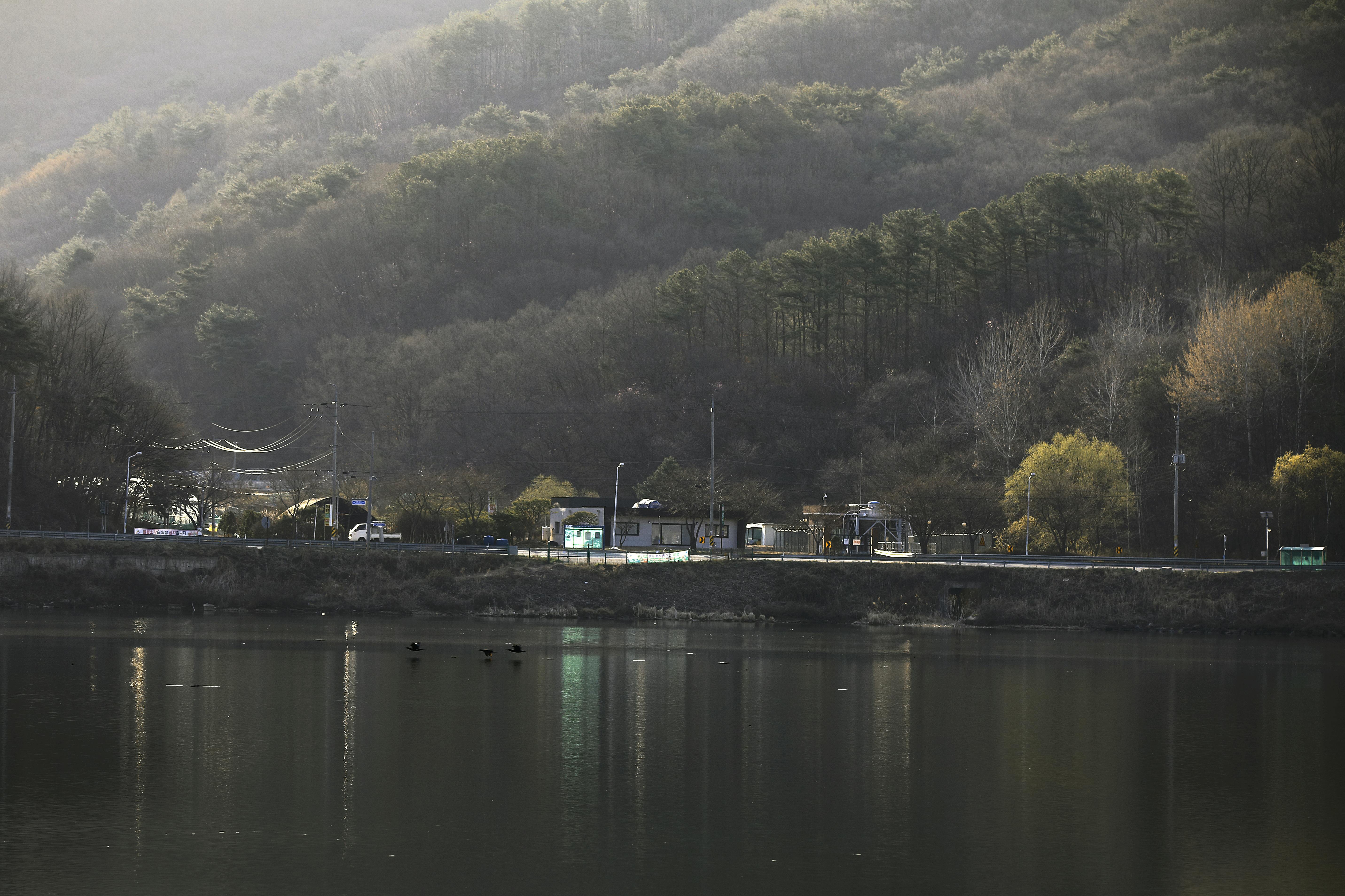 Tranquil lakeside scene in Namyangju-si, Gyeonggi-do, South Korea, surrounded by lush hills and serene water.