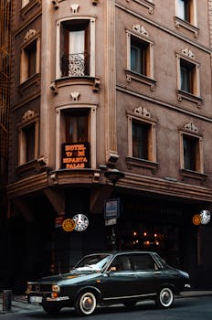 A classic car parked near a historic hotel facade on an urban city street corner.