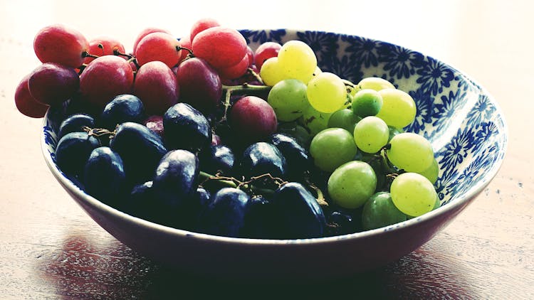 Red, Black, And Green Grapes In Round Blue And White Floral Ceramic Bowl