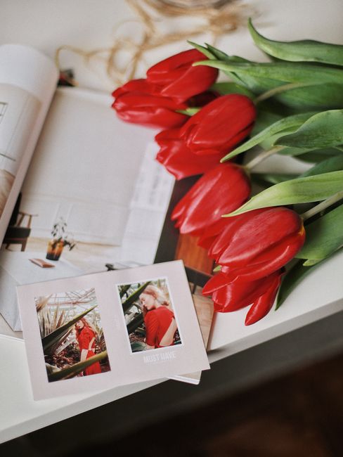 Aesthetic arrangement of red tulips with a magazine and photographs on a table.