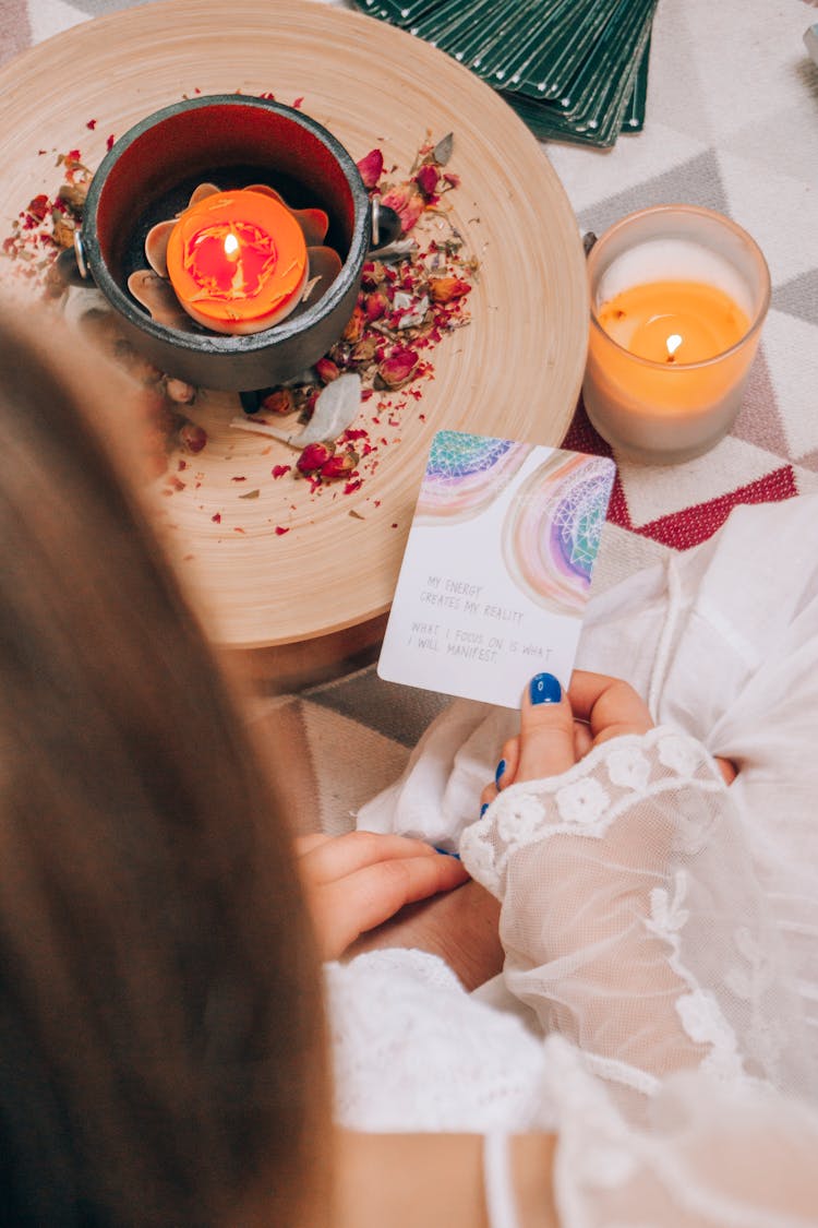 Woman Holding A Card And Sitting Next To Burning Candles