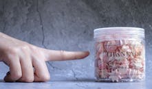 一只手指着一个罐子，罐子里装满粉红色蛋白酥皮饼干，上面写着感谢信息