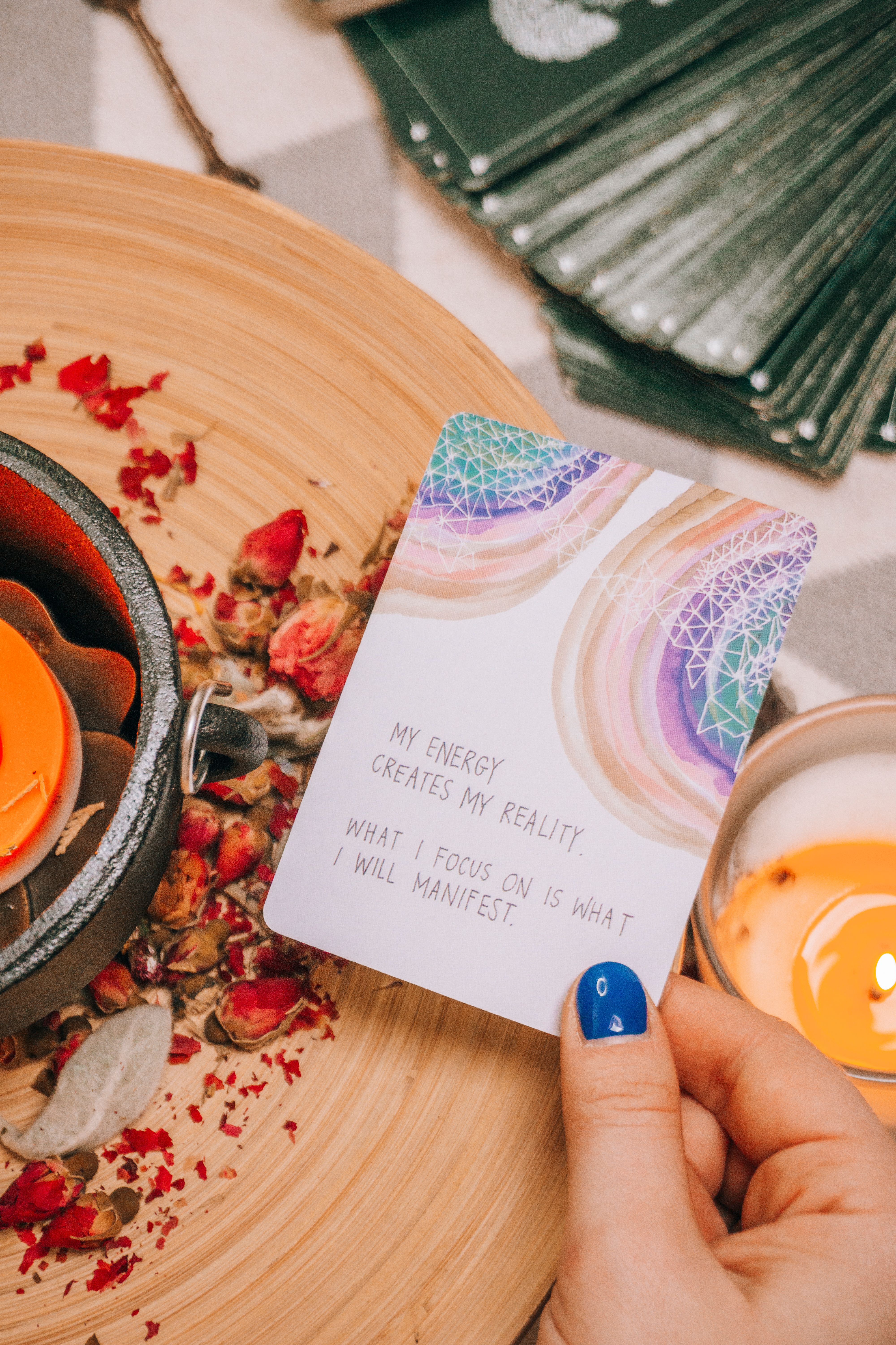 A hand holding an inspiring card next to a candle on a wooden table, surrounded by floral decor.