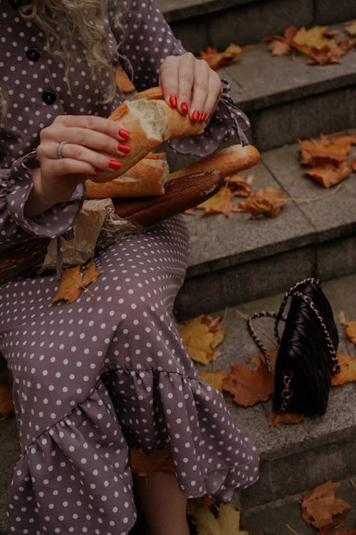 A Woman in Polka Dot Dress Sitting on the Stairs while Holding a Bread