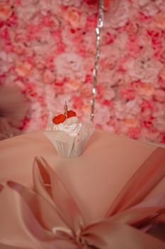 A stylish cupcake with raspberries and whipped cream on a wrapped gift, set against a pink floral backdrop.