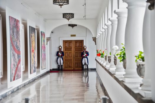 This museum corridor features art displays, guards, and elegant architecture.