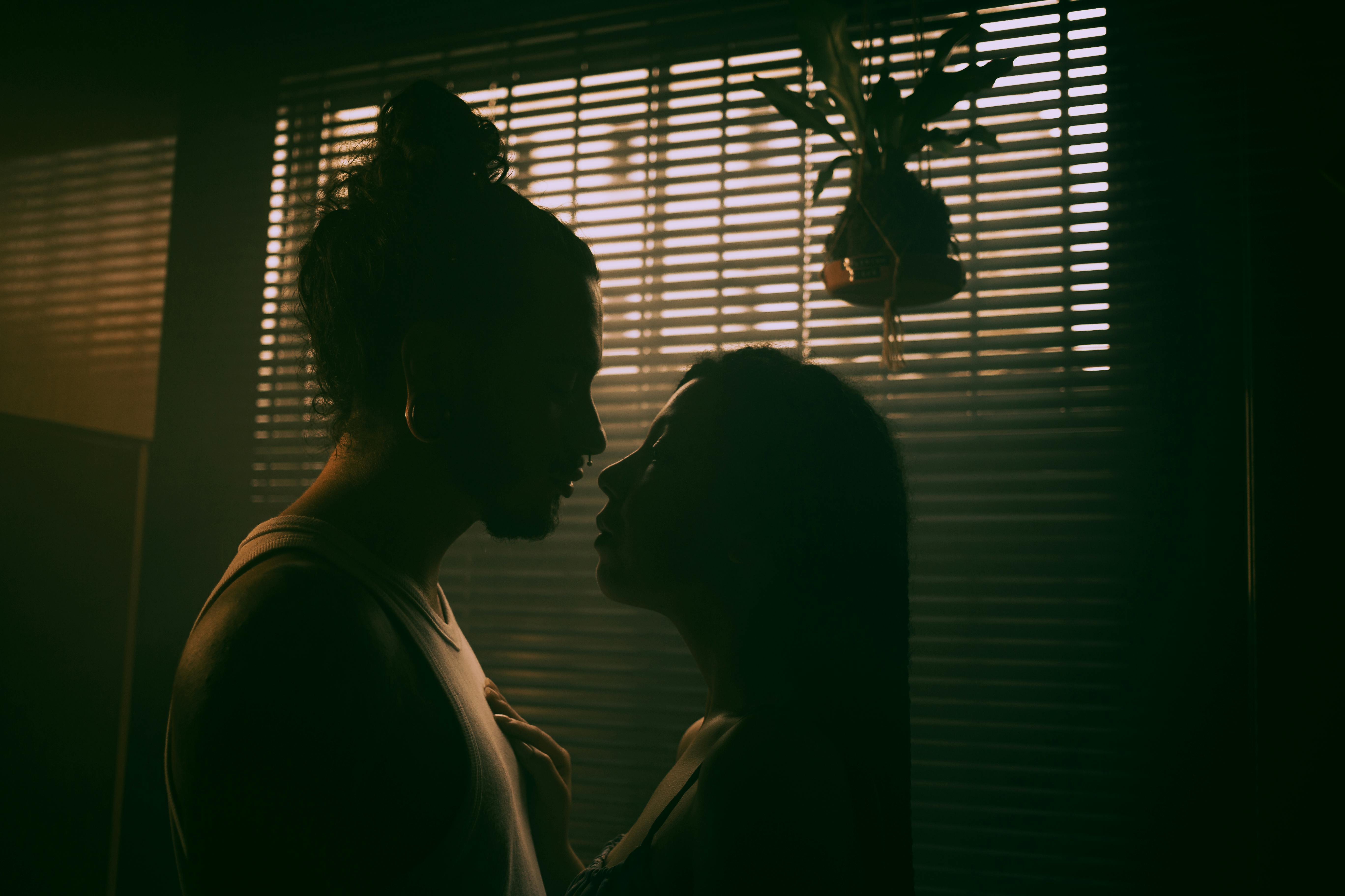 Intimate silhouette of lovers close in dim room, faces inches apart in sensual anticipation