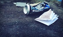 皱巴巴的饮料罐和纸张散落在城市街道上，凸显了环境问题