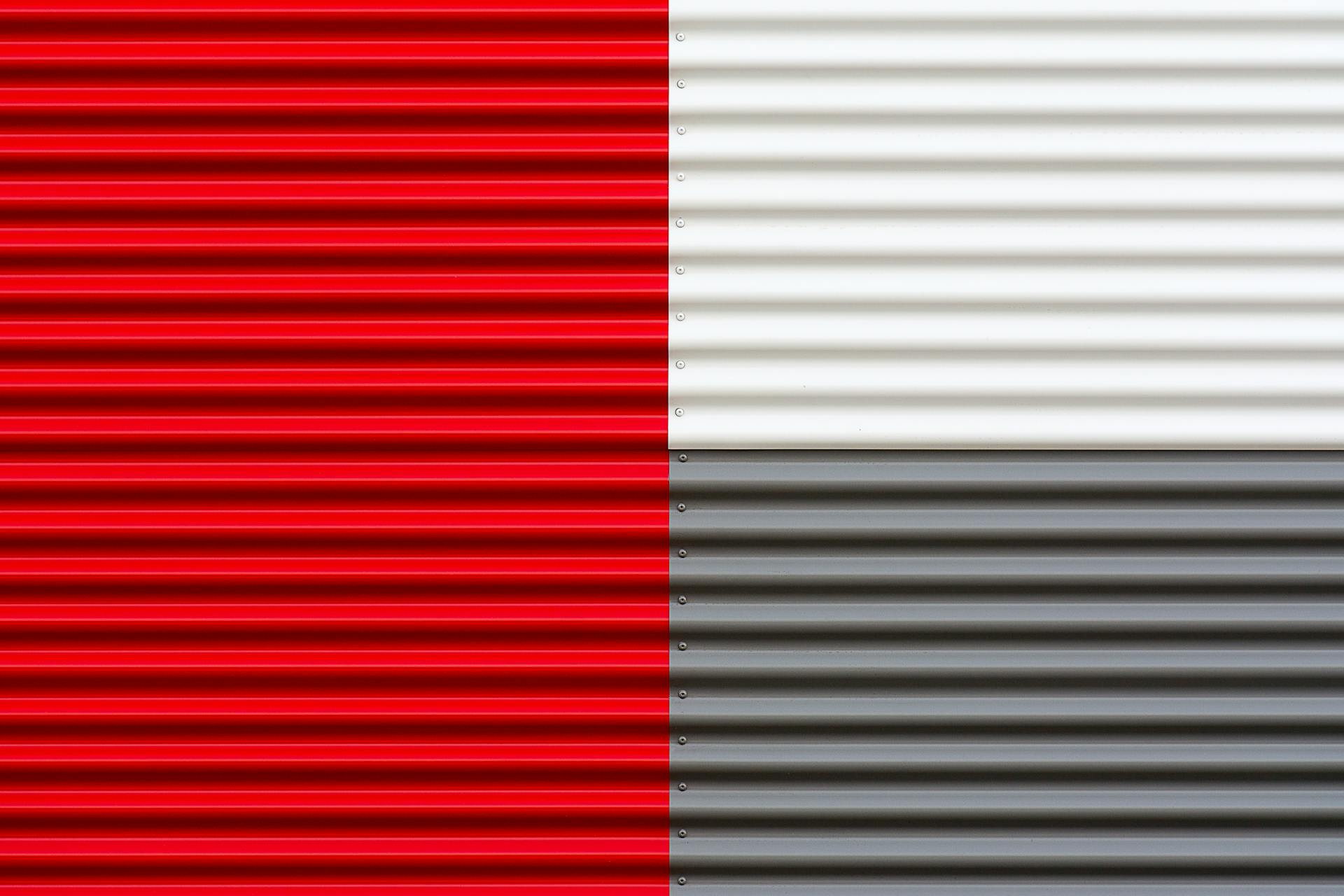 Close-up of red, white, and gray corrugated metal sheets forming a geometric pattern.