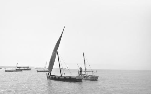 Grayscale Photo of a Person Riding a Sailboat on the Ocean under the Sky