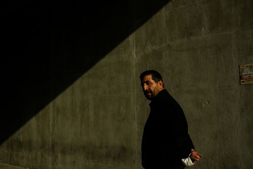 Free A man looks back with dramatic shadows cast on a concrete wall, creating a moody urban scene. Stock Photo