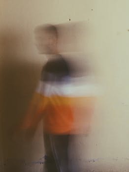 Blurred abstract photo of a man in casual clothing walking indoors, capturing motion.