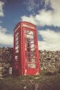 在多云的天空下，经典的红色电话亭被石墙和草地环绕