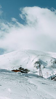 Serene winter landscape featuring a snow-covered mountain and a rustic chapel under white clouds.