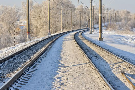 Curved train tracks in a snowy landscape during winter, with power lines and trees.