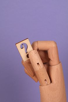 A wooden mannequin hand holding a puzzle piece with a question mark on a violet background.