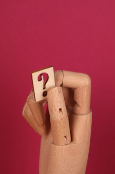 A wooden mannequin hand holds a block with a question mark on a red background.