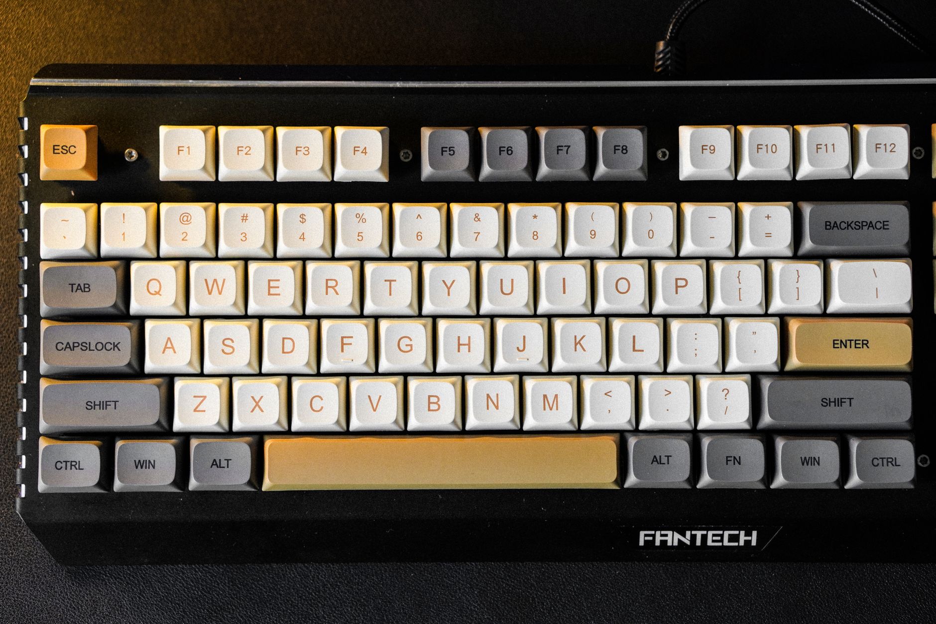Close-up of a mechanical keyboard with custom Fantech keycaps in a color mix of beige, gray, and white.