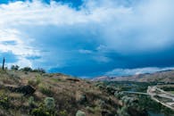 在动态多云的天空下，连绵起伏的山丘、郁郁葱葱的绿植和远处的桥梁构成了一幅令人惊叹的画卷