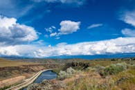 在明亮的蓝天下，广阔的河流蜿蜒穿过山谷，蓬松的云朵展示了大自然的美丽