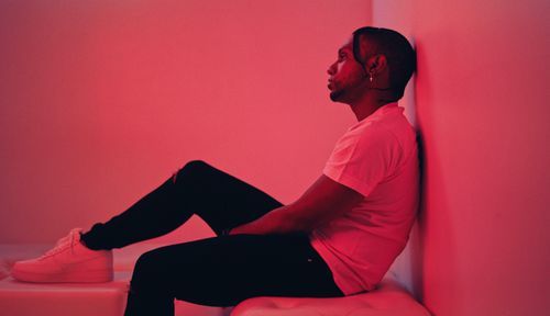 Free Side profile of a man sitting thoughtfully against a red wall in an artistic setting. Stock Photo