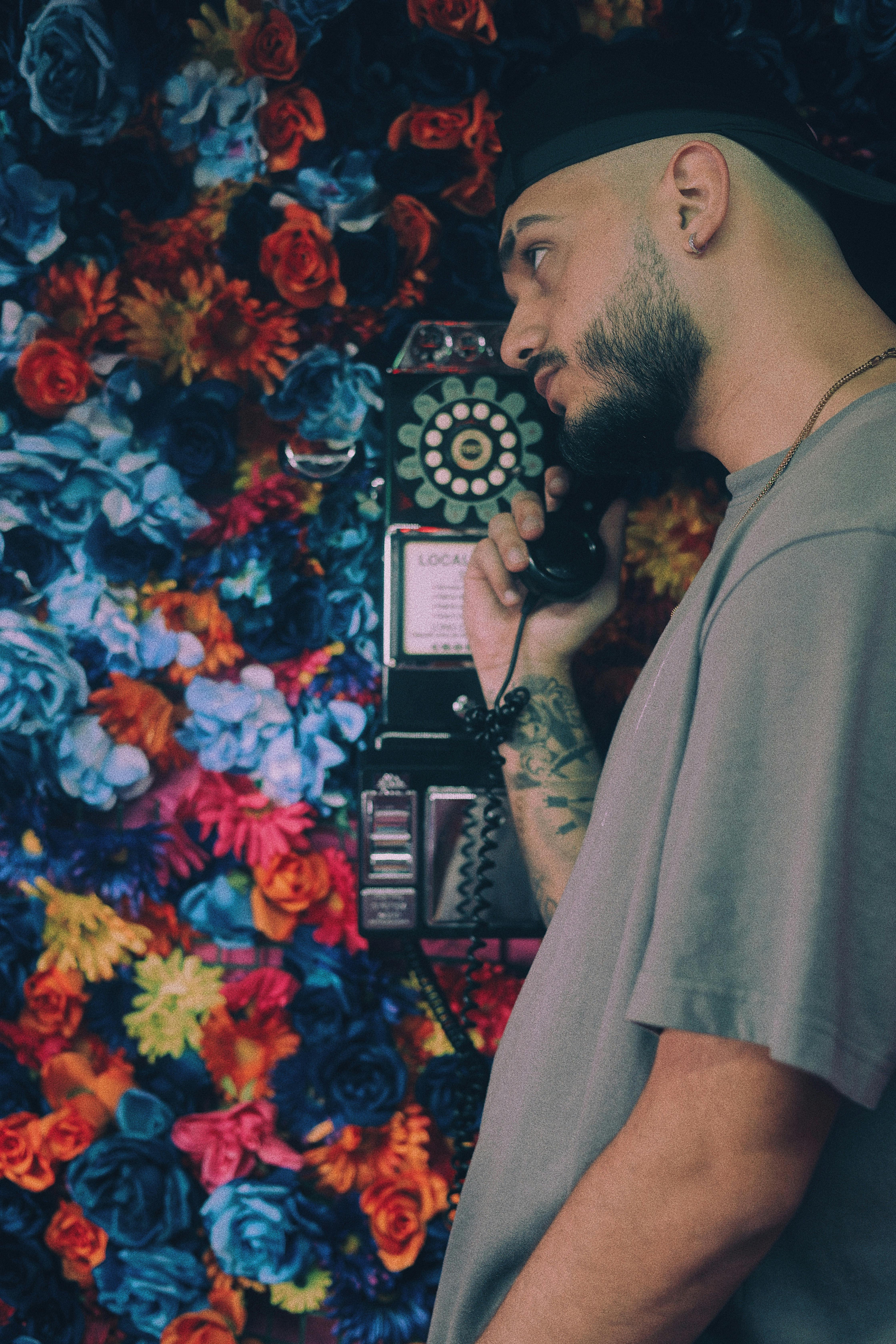 Side profile of a man using a vintage phone, surrounded by a colorful flower wall.