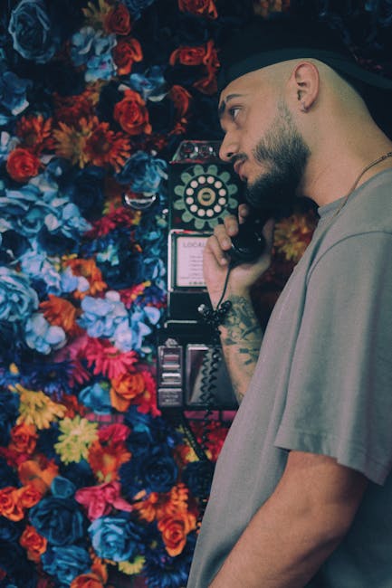 Side profile of a man using a vintage phone, surrounded by a colorful flower wall.