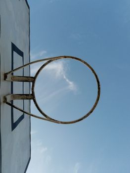 An aged basketball hoop photographed from a low angle against a clear sky.