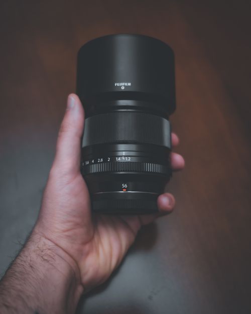 Free A close-up of a hand holding a Fujifilm camera lens on a soft-focus background. Stock Photo