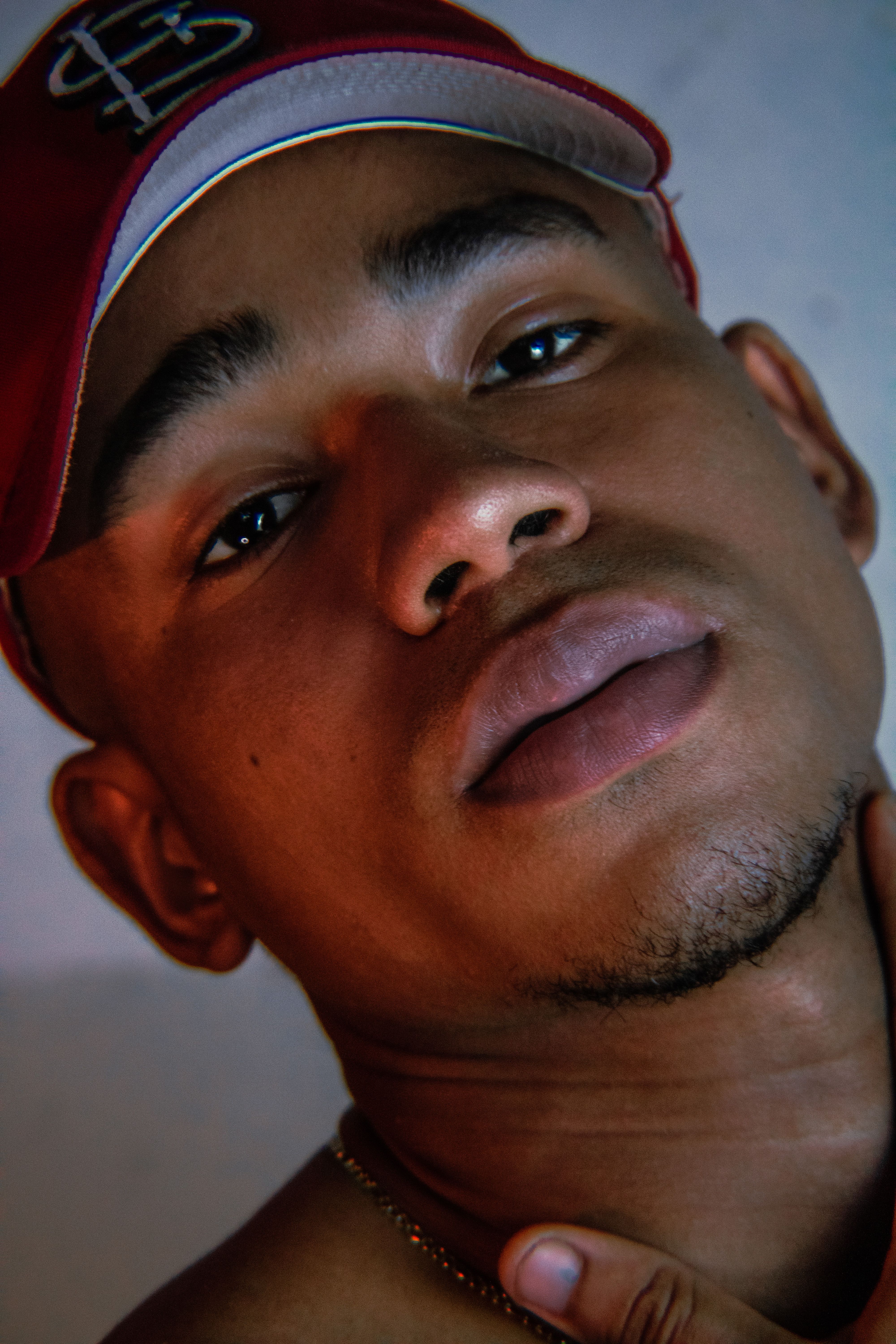 Intimate close-up portrait featuring a young man wearing a red cap, highlighting his expressive eyes and goatee.